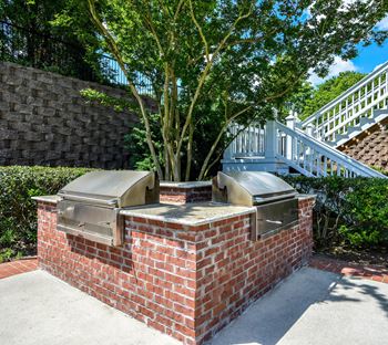 A brick barbecue with two bbq grills and a tree in the background
